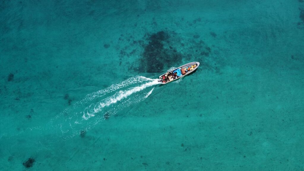 Aerial view of a small boat cruising over the clear turquoise waters of Milne Bay, Papua New Guinea.